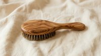 Wooden hair brush with natural bristles on soft beige fabric background for spa and beauty care routine.