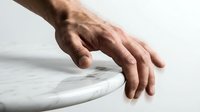 Male hand with medium skin tone touching white marble surface, isolated on light background for design mockups and product presentations.