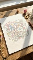 Thank you you card with hand-lettered text surrounded by decorative florals and botanical elements on wooden surface with dried flowers.