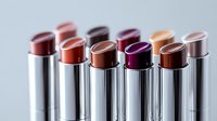 Colorful array of metallic lipstick tubes arranged in line showing variety of trendy shades from nude to deep purple, macro shot with soft focus background.