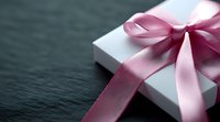 White gift box with pink satin ribbon bow on dark stone background, selective focus. Elegant present packaging for special occasions and holidays.