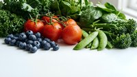 Fresh organic vegetables and fruits including broccoli, spinach, peas, cherry tomatoes and blueberries arranged on white background for healthy eating.