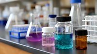 Laboratory glassware with colorful liquid chemicals in glass bottles and flasks on lab bench, scientific research equipment in modern facility background.