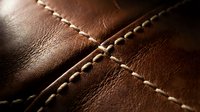 Brown leather texture with decorative stitching seams creating geometric pattern. Close-up macro shot showing craftsmanship details for luxury goods design.