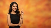 Young Indian woman in black top pointing upward with finger against warm orange background for advertising and promotional content.