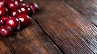 Fresh ripe red cherries scattered on rustic wooden table background with copy space. Natural lighting creates dramatic shadows on textured surface.