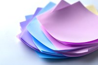 Colorful stack of curved paper sheets in pastel pink, purple, and blue tones creating abstract layered composition against white background. Suitable for office and craft designs.