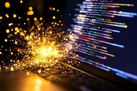 Programming code on computer screen with explosive golden light effect and bokeh, representing digital transformation and technological breakthrough.