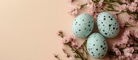 Pastel mint green speckled Easter eggs arranged with delicate pink cherry blossom branches on soft peach background, creating seasonal spring composition.