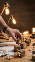 Male hand arranging wooden blocks with lightbulb icons on workshop table surrounded by vintage Edison bulbs and blueprints for creative business planning.