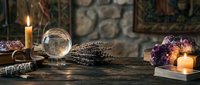 Mystical fortune telling setup with crystal ball, candles, amethyst crystals and dried lavender on rustic wooden table for spiritual divination practices.