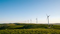 Renewable energy wind turbines on rolling green hills under clear blue sky, suitable for sustainable power and environmental projects.