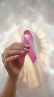 Woman hand holding pink ribbon symbol for breast cancer awareness campaign with soft bokeh light background for healthcare support concept.
