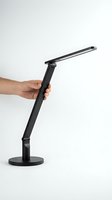 Caucasian male hand holding a sleek black LED desk lamp on white background, showcasing modern adjustable lighting for home office use.