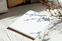 Blank white notebook with natural shadow overlay from tree branches on textured fabric background, creating minimalist composition for creative design projects.