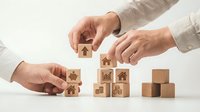 Business hands arranging wooden blocks with real estate icons representing property investment, mortgage planning and housing market growth strategies.