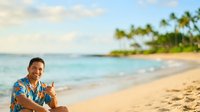 Man in colorful Hawaiian shirt relaxing on tropical beach with palm trees and turquoise ocean water, vacation and travel lifestyle concept for resort and leisure design projects.