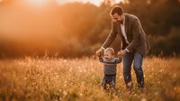 Father and toddler son playing together in golden sunset field, warm family bonding moment outdoors in nature during golden hour for parenting concepts.