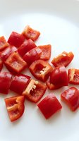 Fresh red bell pepper pieces chopped and diced on white background for cooking ingredients and healthy food preparation.