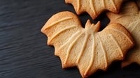Homemade maple leaf shaped butter cookies with delicate ribbed texture on dark wooden background, autumn baking concept for seasonal treats.
