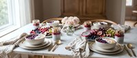 Elegant dining table set with fresh flowers, grapes, and fine dinnerware creating warm inviting atmosphere for special occasions and gatherings.