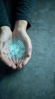 Caucasian hands cupped together displaying glowing shield security hologram symbol on palm against dark textured surface, representing data protection and cybersecurity technology.