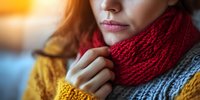 Close up portrait of woman wearing cozy knitted red scarf and yellow sweater on blurred background with warm sunlight. Soft focus winter fashion concept.