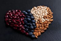 Heart shape made of fresh blueberries, raw almonds and red kidney beans arranged on dark background, healthy eating concept for Valentine's day.