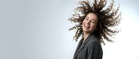 Joyful mixed-race businesswoman with curly hair in motion, laughing with dynamic hair movement against neutral background for corporate branding.