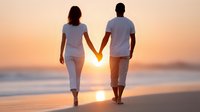 Romantic couple holding hands walking on beach at sunset with golden sky and ocean waves creating peaceful moment for love and relationship concepts.