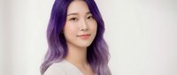 Young Asian woman with vibrant purple hair smiling confidently in casual white top against soft neutral background for lifestyle content.