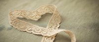Delicate cream lace ribbon arranged in heart shape on soft fabric background for romantic wedding decoration and craft projects.