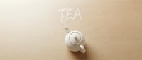 White ceramic teapot on wooden surface with steam forming the word TEA, top view flat lay, cozy morning drink concept.