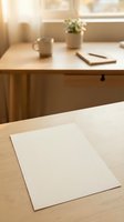 Blank white paper sheet on wooden desk in bright sunlit workspace with coffee mug, notebook, and potted plant for mockup and branding projects.