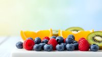 Fresh mixed berries and kiwi slices on white surface with colorful gradient background for healthy eating and nutrition concepts.