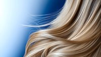 Flowing blonde hair strands on blue background, soft focus close-up showing natural movement and shine. Professional hairstyling and beauty concept.