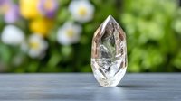 Clear quartz crystal point standing upright on gray surface with soft floral bokeh background creates serene spiritual atmosphere for wellness and meditation.