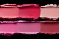 Smeared lipstick samples in various pink and red shades on black background showing texture and pigment intensity of cosmetic products.