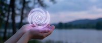 Hands holding glowing pink spiral energy orb at twilight lake with mountains and trees in background for wellness and spiritual concepts.