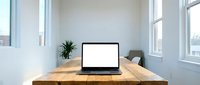 Minimalist home office workspace with open laptop on wooden desk near large windows. Clean modern interior design for remote work and productivity.