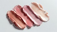Cosmetic lipstick or cream blush swatches in gradient shades from peach to pink on white background, showcasing makeup texture for beauty product photography.