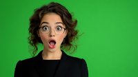 Young Hispanic woman with glasses and curly hair expressing surprise with open mouth against green background, wearing black blazer. Professional headshot for business.