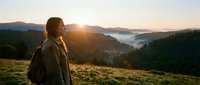 Woman hiker with backpack enjoying sunrise over misty mountain valley landscape, outdoor adventure and nature exploration.