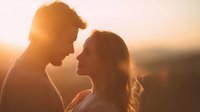 Romantic couple silhouettes embracing at golden hour sunset with warm sunlight creating intimate backlit scene for love and relationship concepts.