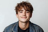 Young man with curly brown hair and light complexion wearing denim shirt over black top, smiling at camera against white background for portrait use.