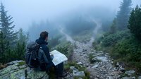 Hiker with backpack reading map on misty mountain trail surrounded by evergreen forest and fog for outdoor adventure and navigation concepts.