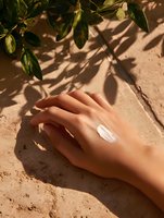 Female hand with moisturizer cream on skin against natural beige background with green leaves and shadow play. Cosmetic and skincare concept.
