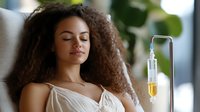 Young mixed race woman with curly hair resting during intravenous vitamin therapy treatment at wellness spa. Medical drip provides hydration and nutrients.