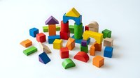 Colorful wooden building blocks scattered on white background, featuring cubes, triangles, cylinders and geometric shapes for educational play and construction.