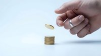 Caucasian hand dropping gold coin onto stack of coins, symbolizing savings, investment, and financial growth on white background.